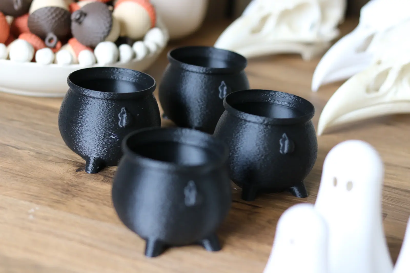 Four small black cauldrons on a wooden table.