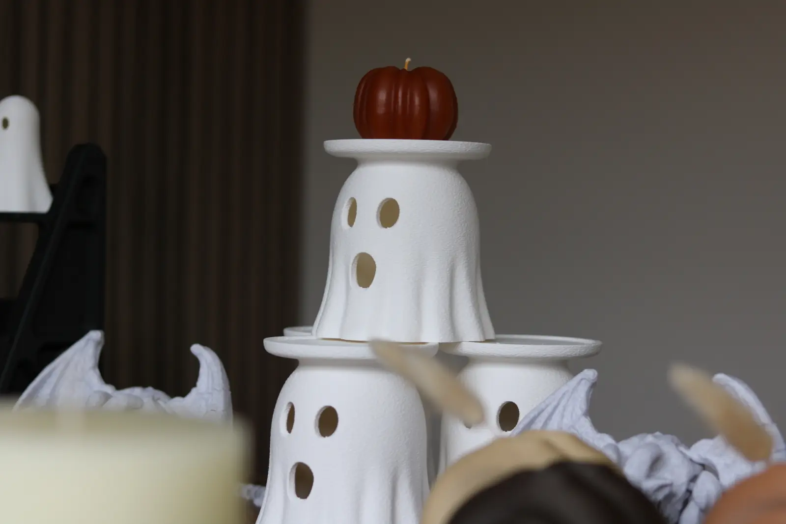 Stacked white ghost candle holders with a pumpkin candle on top.