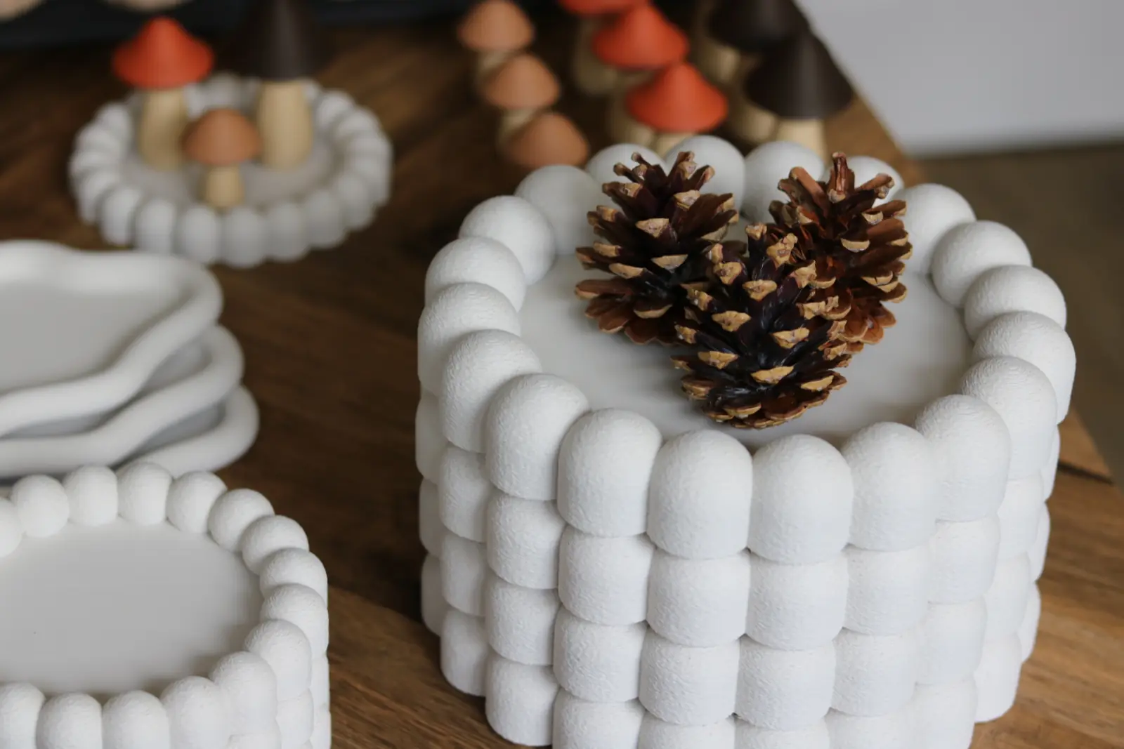 A white beaded vessel with pinecones on top.